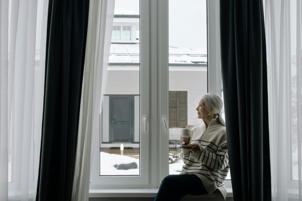 femme regardant la neige par la fenêtre de sa maison